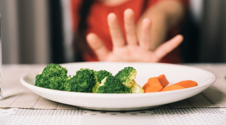 child's hand refusing a plate of vegetables