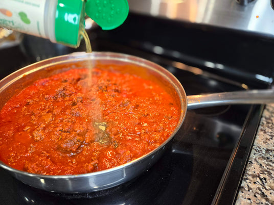 Easy Peasie veggie powder Green Blend being sprinkled into a pot of spaghetti sauce on the stove